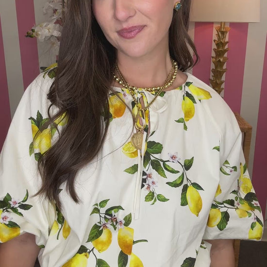 Woman wearing a white blouse with lemon print in a room with pink and white striped wallpaper.