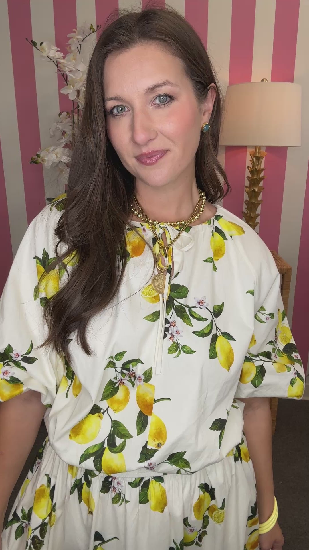 Woman wearing a white blouse with lemon print in a room with pink and white striped wallpaper.