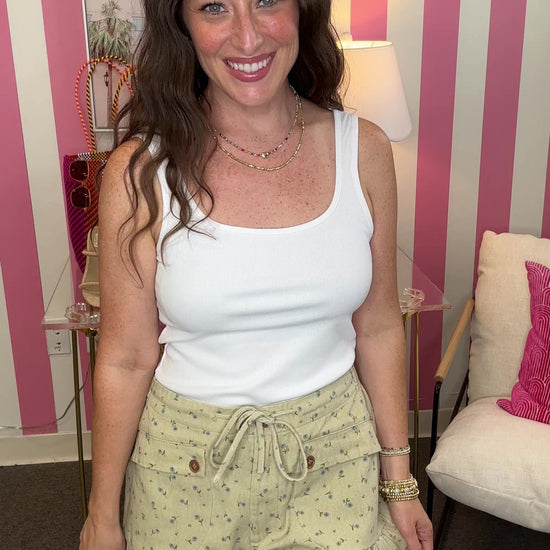 Woman wearing a white tank top and light green shorts in a room with pink walls.