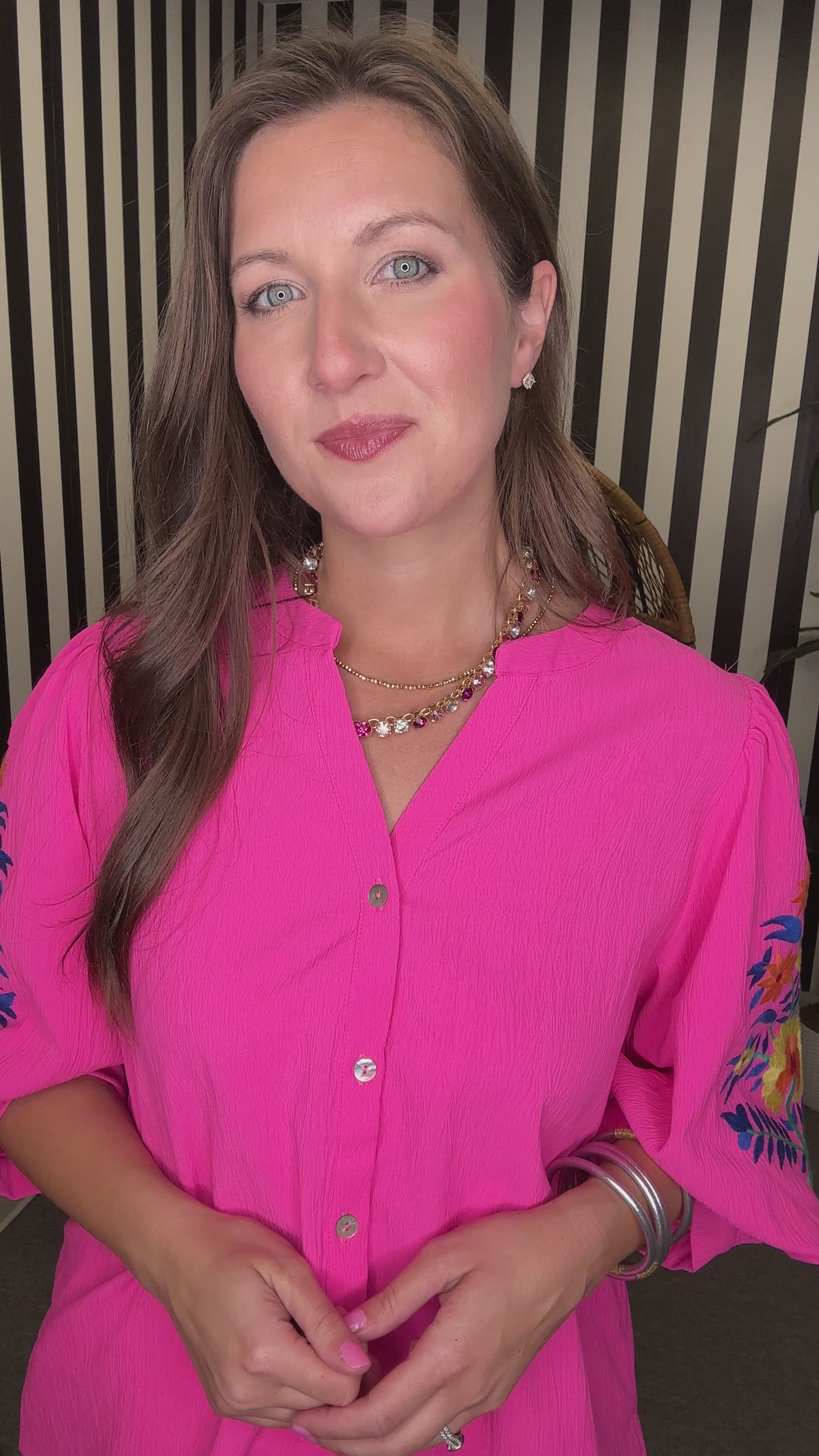 Woman wearing a bright pink blouse with floral sleeves indoors.