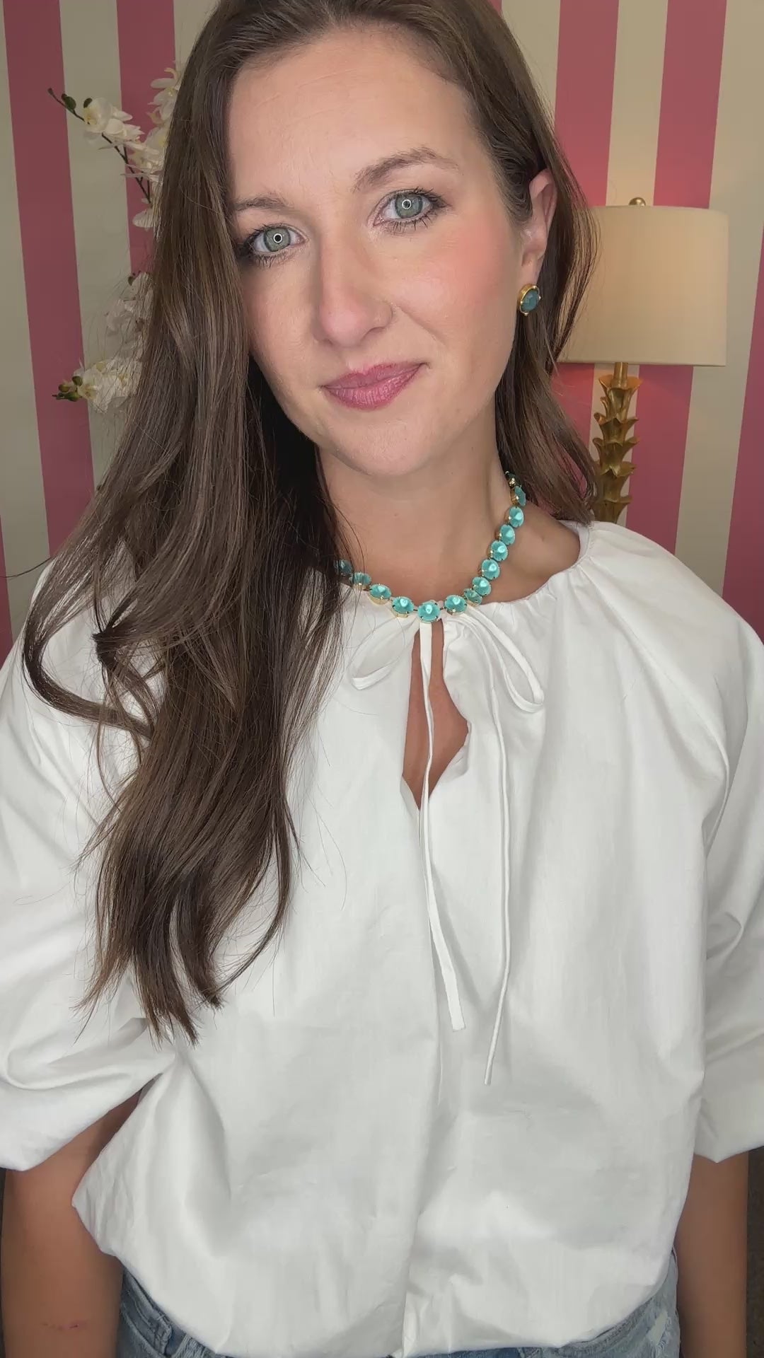 Woman wearing a white blouse and denim shorts in a room with striped wallpaper.