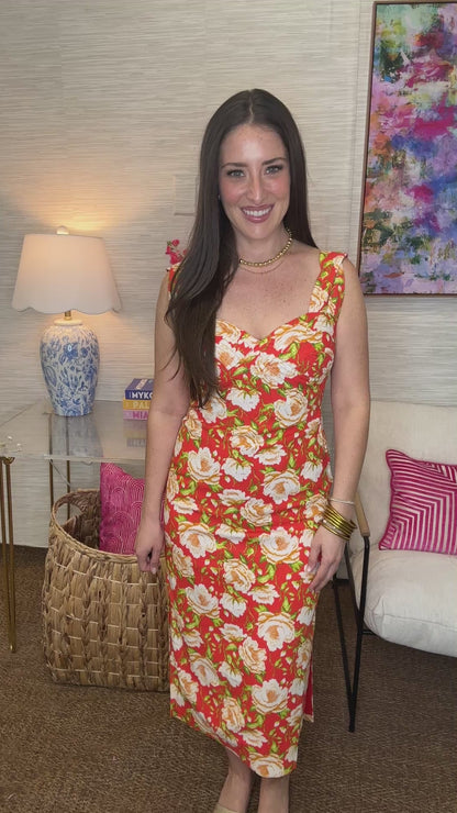 Woman in a colorful floral dress standing in a living room with a couch and lamp.