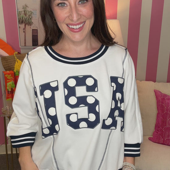 Woman wearing a white sweatshirt with 'USA' printed on it in a casual setting.