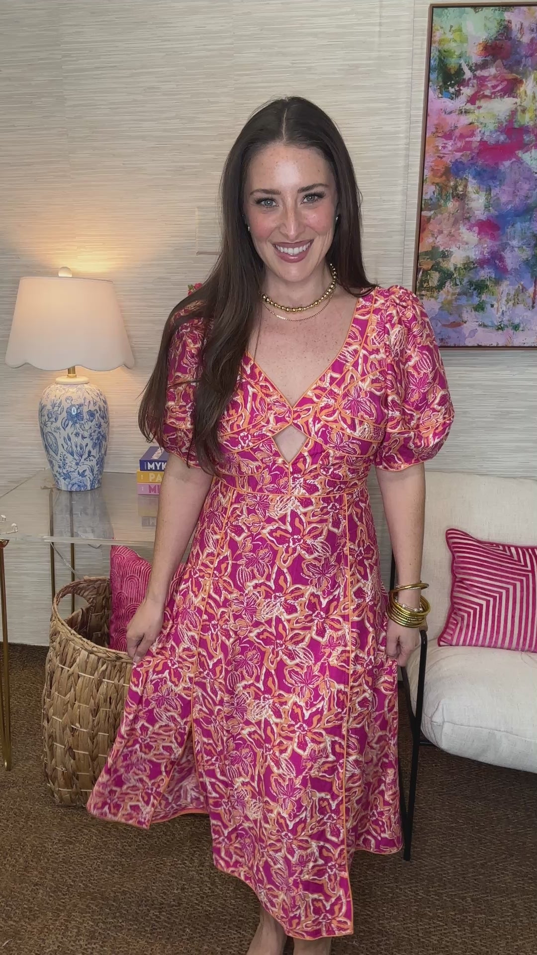 Woman in a pink floral dress standing in a living room with a colorful painting on the wall.