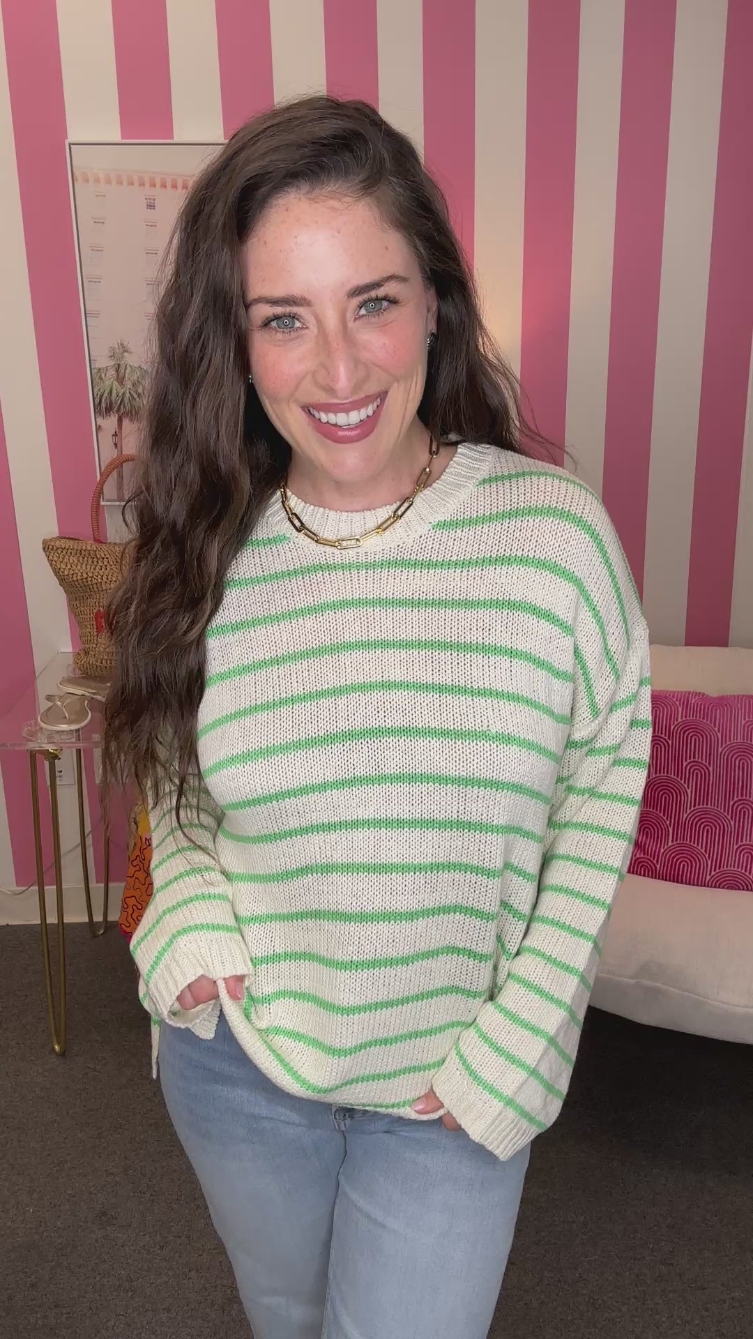 Woman wearing a green and white striped sweater in front of a pink and white striped wall.