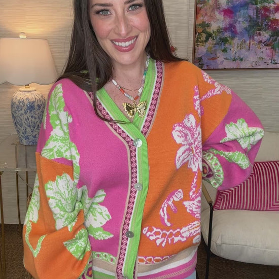 Woman wearing a colorful floral-patterned jacket in a room with a lamp and painting.