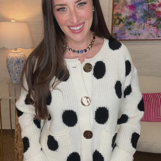 Woman wearing a white cardigan with black polka dots in a room setting.