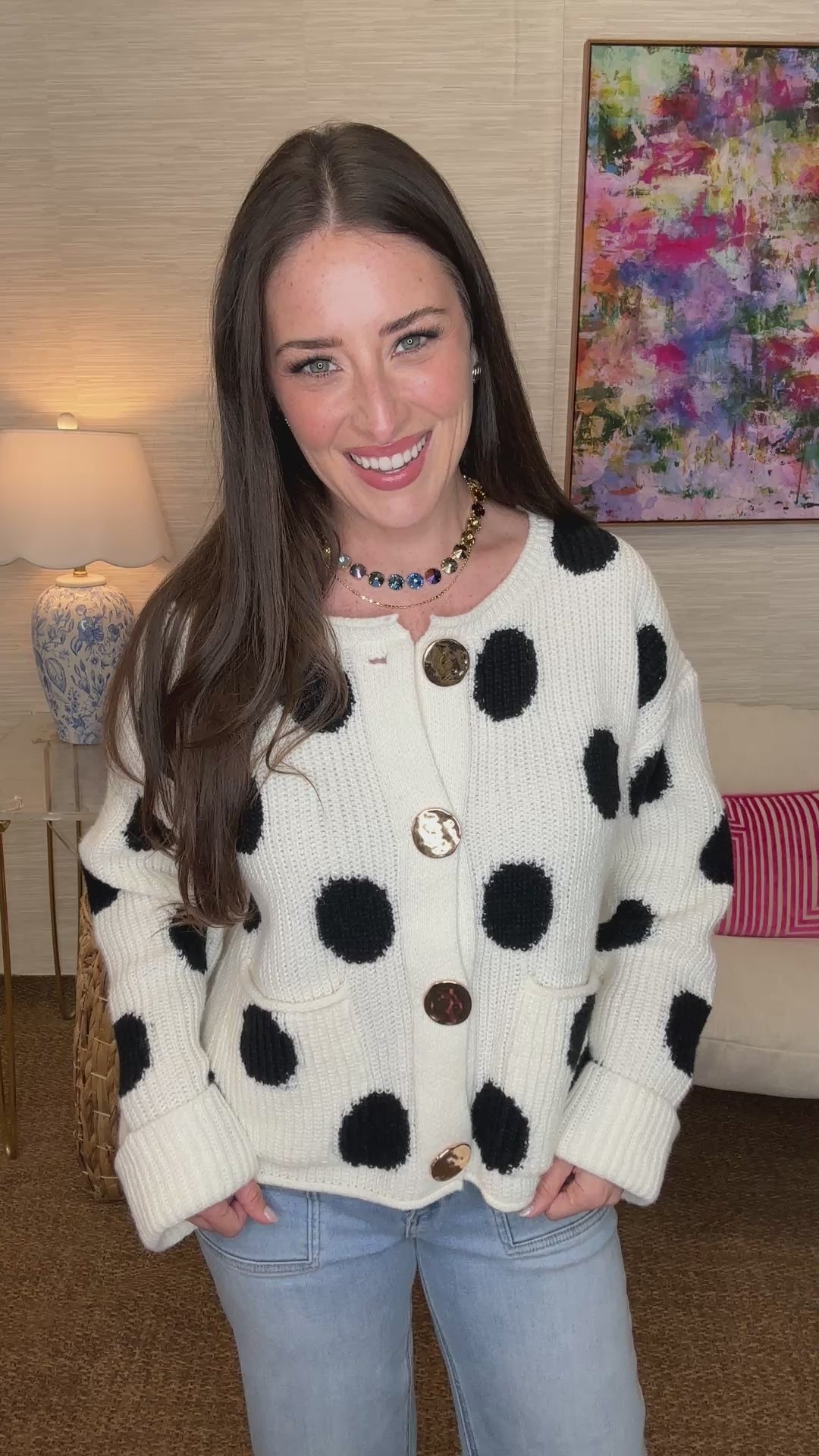 Woman wearing a white cardigan with black polka dots in a room setting.