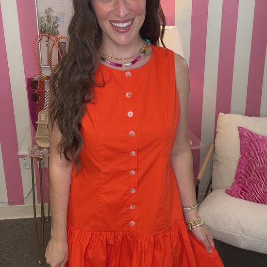 Woman wearing an orange dress in a room with pink and white striped walls.