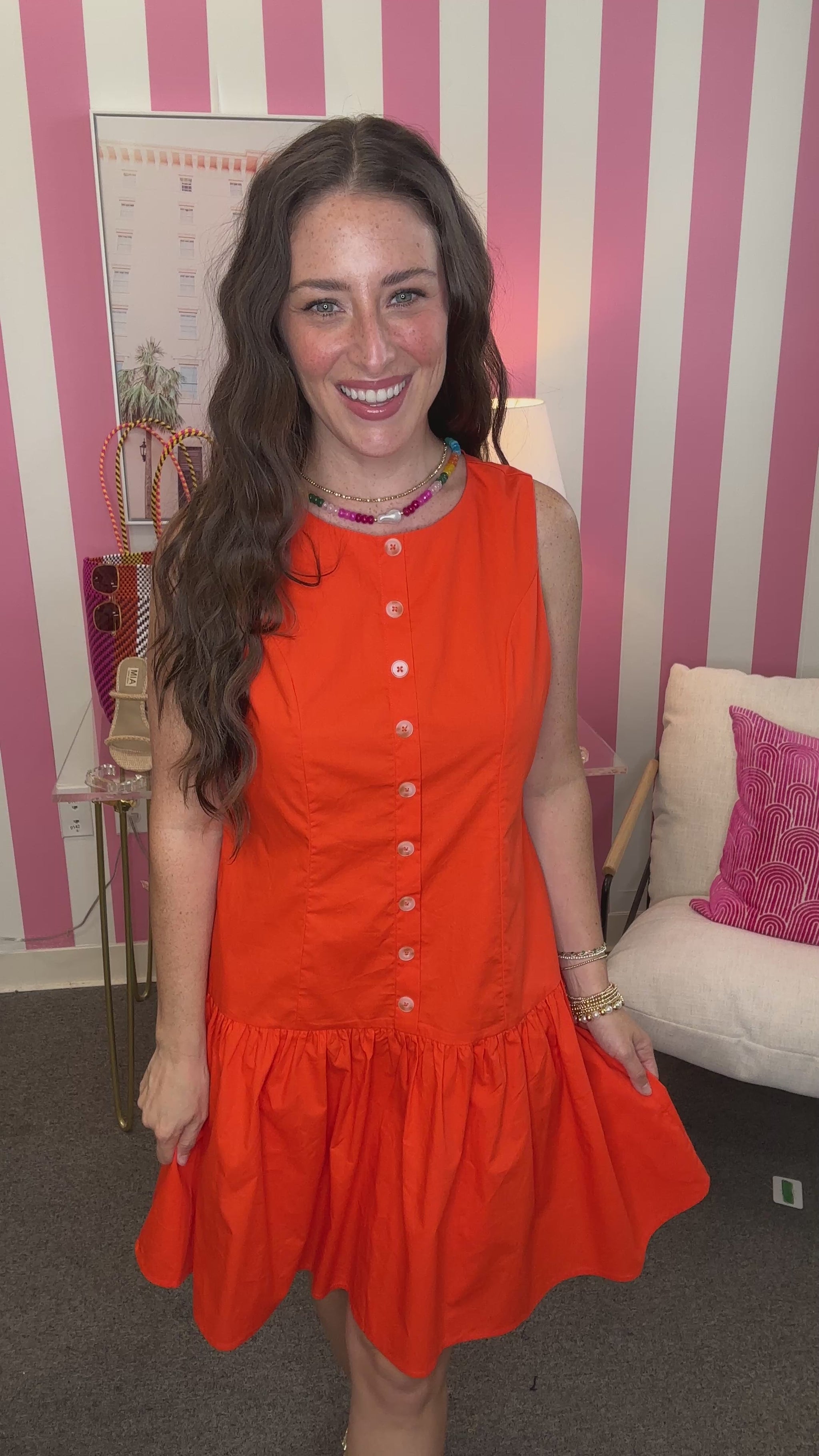 Woman wearing an orange dress in a room with pink and white striped walls.