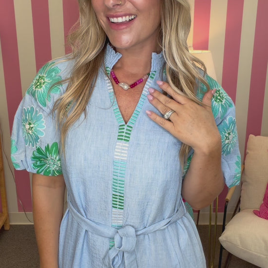 Woman in a light blue dress standing in a room with pink and white striped walls.