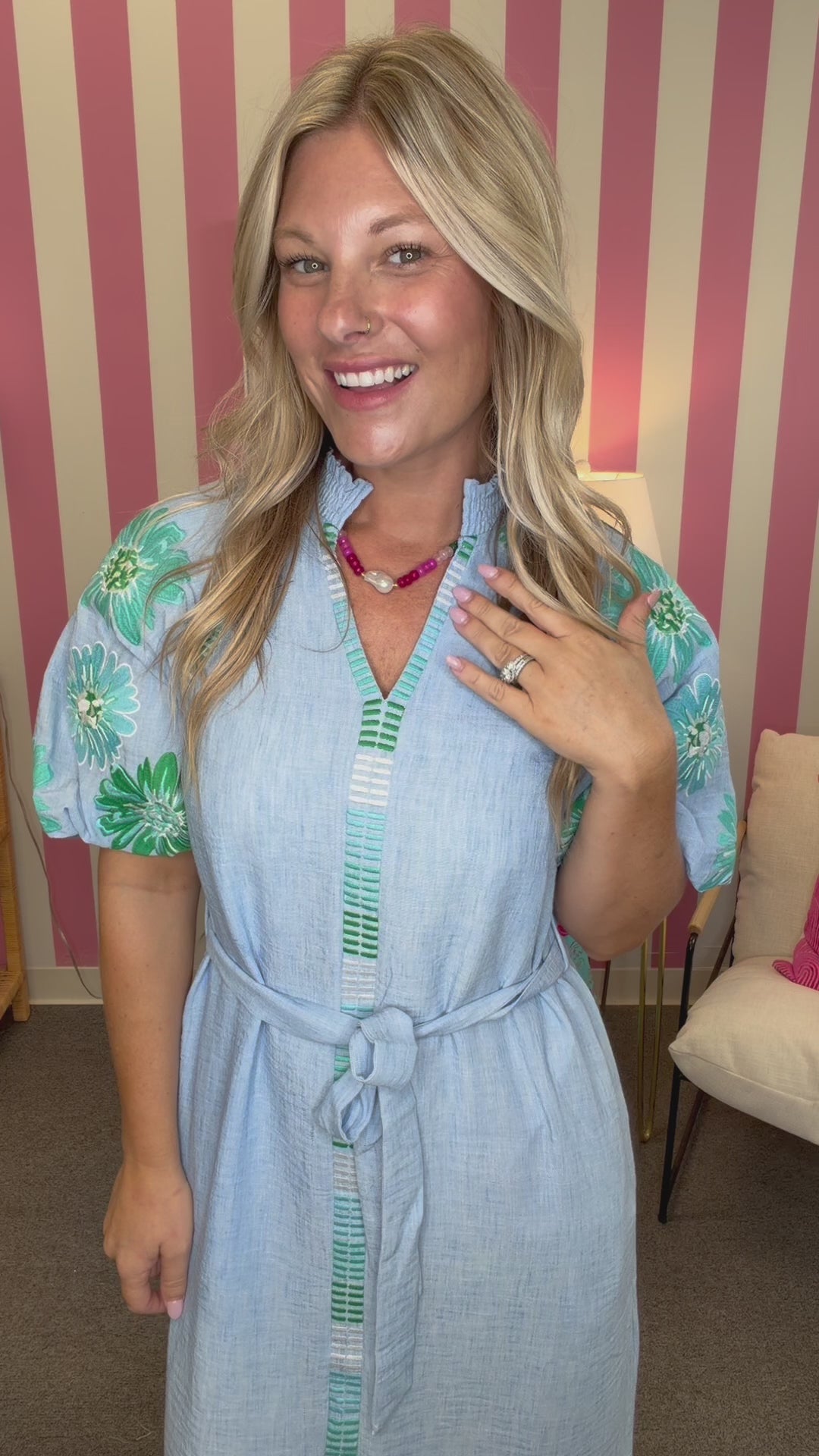 Woman in a light blue dress standing in a room with pink and white striped walls.