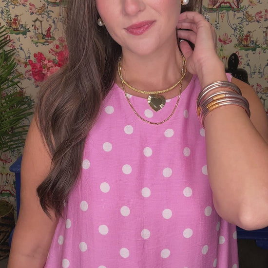 Woman in a pink polka dot dress standing in front of a colorful wall with floral patterns.