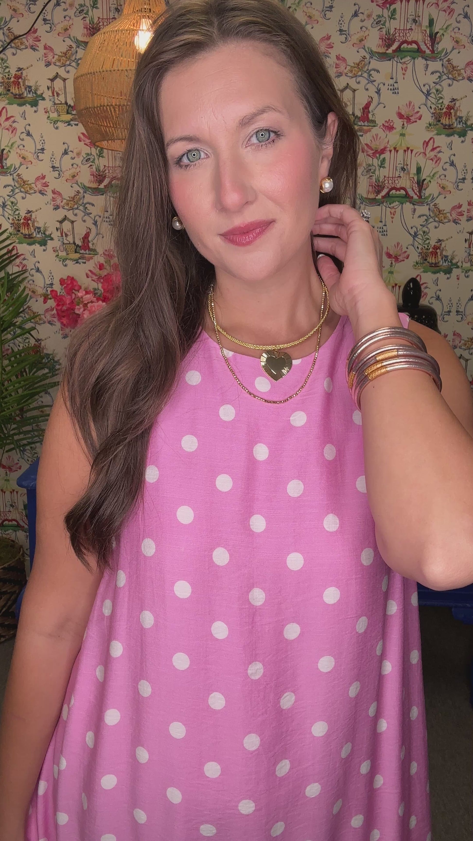 Woman in a pink polka dot dress standing in front of a colorful wall with floral patterns.