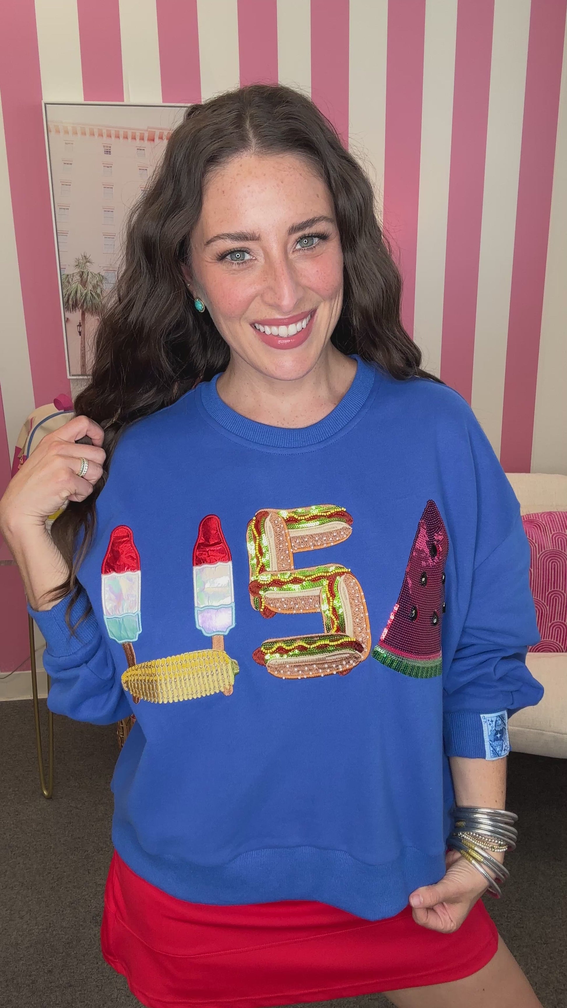 Woman wearing a blue sweatshirt with colorful letters in front of a striped background