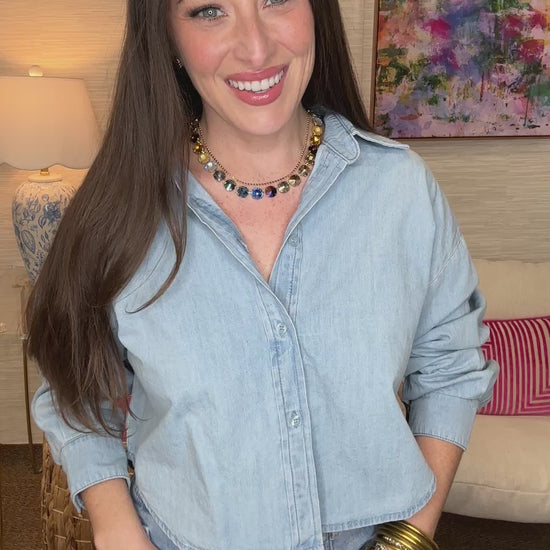 Woman wearing a light blue denim shirt and jeans in a room with a colorful painting on the wall.