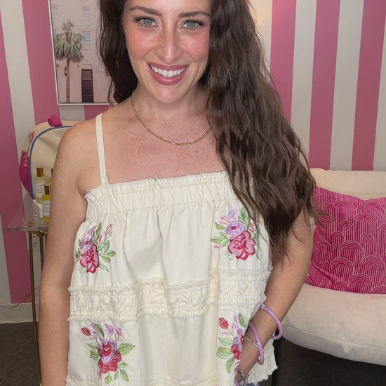 Woman wearing a white blouse with floral embroidery in a room with pink and white striped curtains.