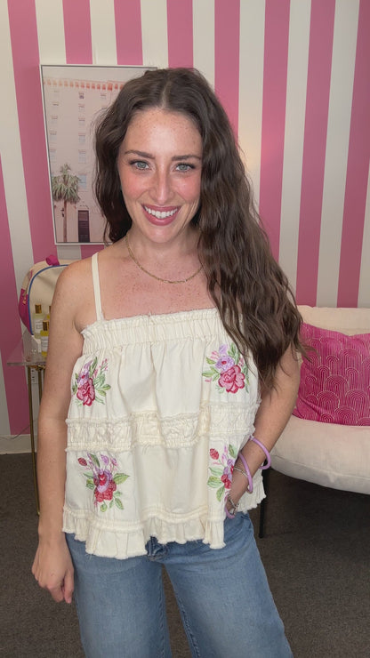 Woman wearing a white blouse with floral embroidery in a room with pink and white striped curtains.