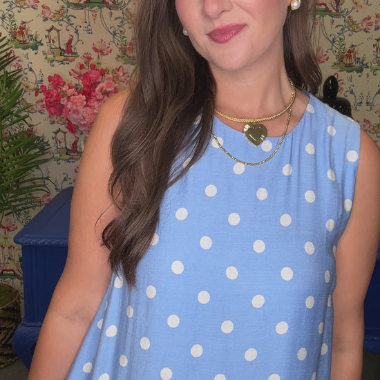 Woman in a blue polka dot dress standing in a room with floral wallpaper and a blue bench.