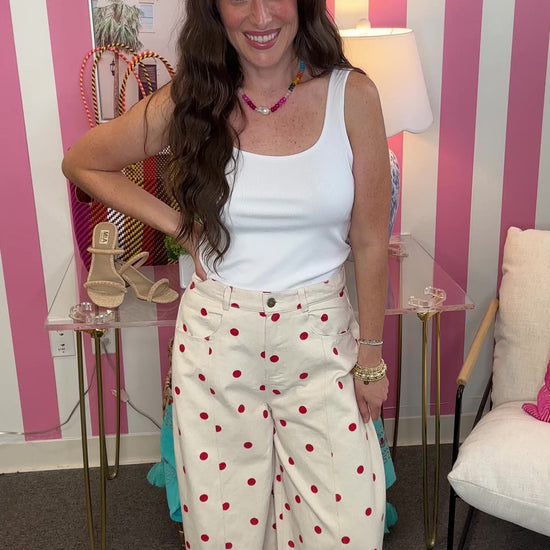 Woman in a white sleeveless top and polka dot pants standing in a room with striped walls and decorative items.
