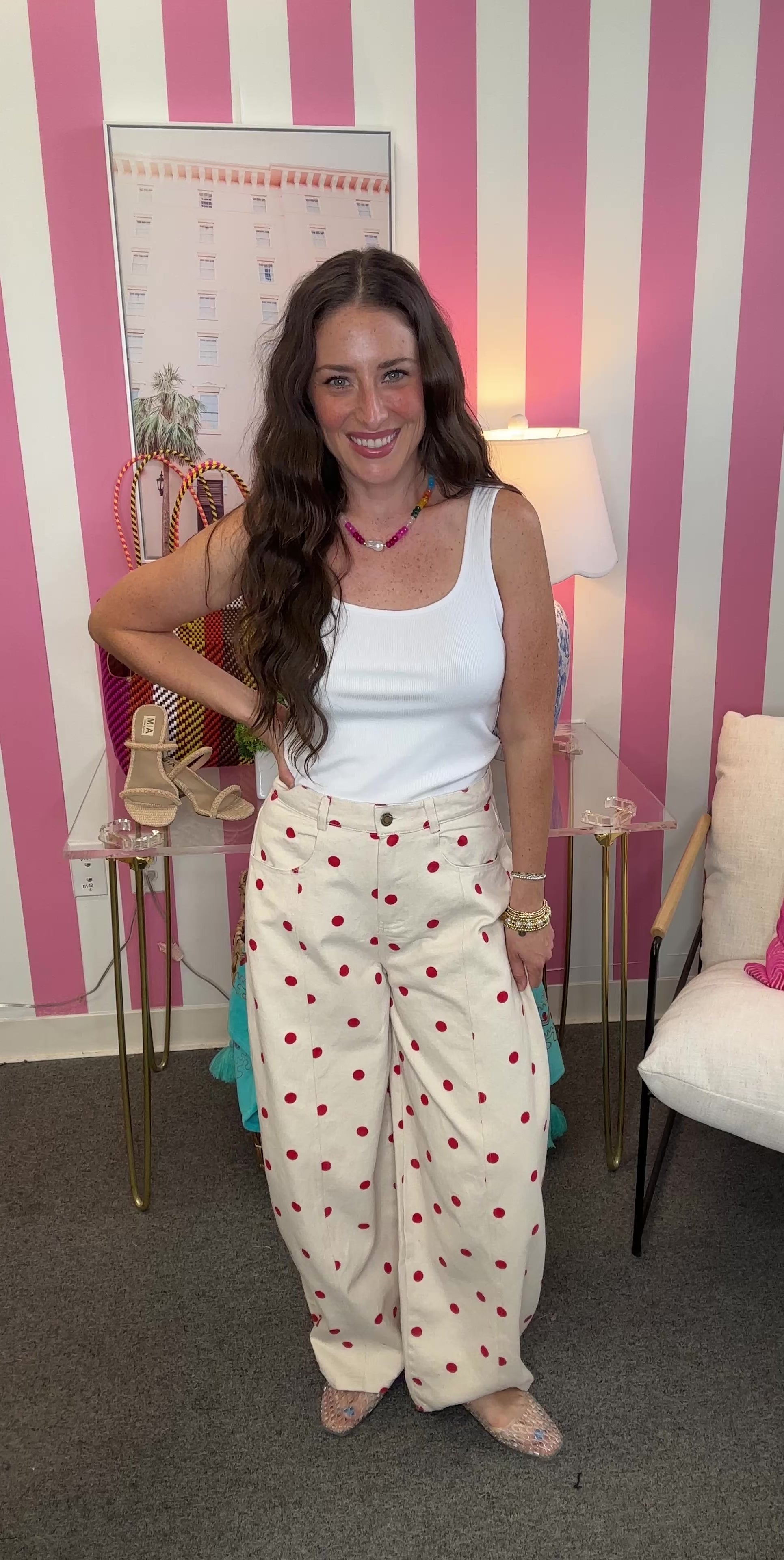 Woman in a white sleeveless top and polka dot pants standing in a room with striped walls and decorative items.