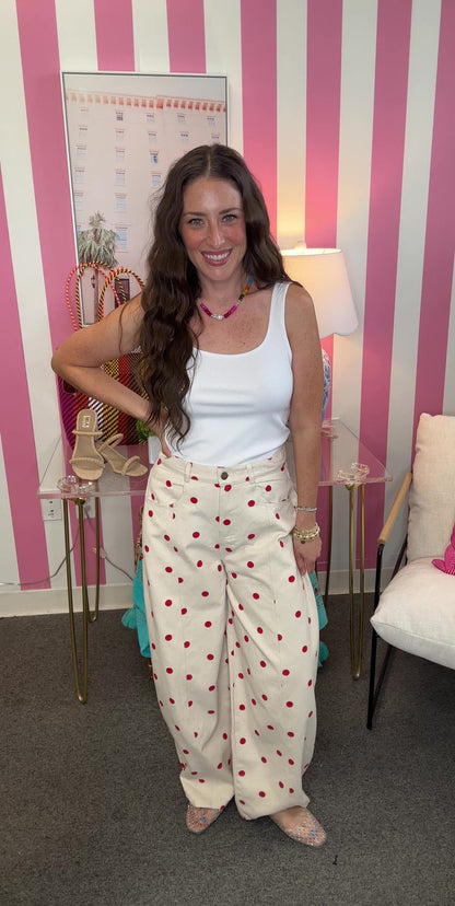 Woman in a white sleeveless top and polka dot pants standing in a room with striped walls and decorative items.