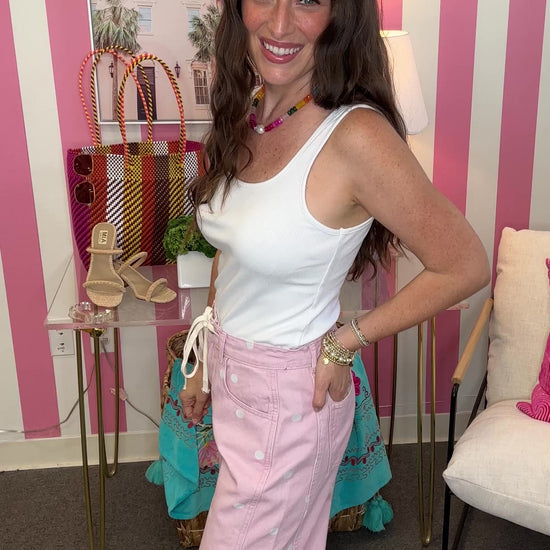 Woman in a white top and pink pants standing in a room with striped walls and furniture.