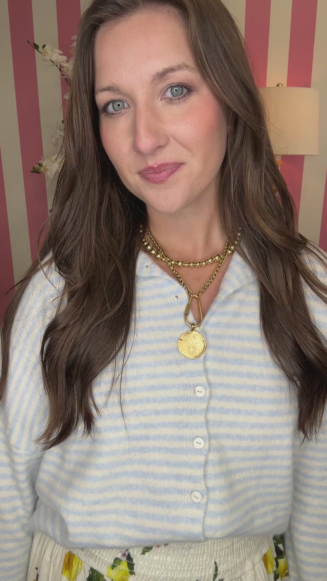 Woman wearing a white top and floral skirt with lemon pattern in a room with striped walls.