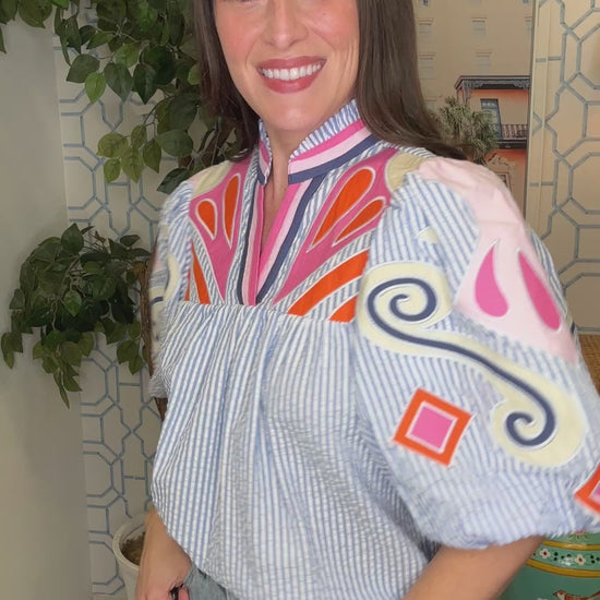 Woman wearing a colorful blouse with puffed sleeves in an indoor setting.