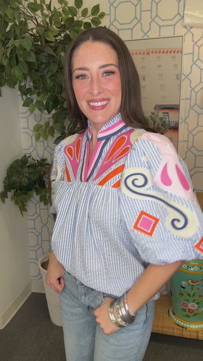 Woman wearing a colorful blouse with puffed sleeves in an indoor setting.